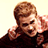 Pixelated static image of a person with light brown hair wearing dark clothing, cropped to show upper body and face against plain background.
