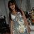 A pixelated image of a woman with long dark hair wearing a light-colored sleeveless dress, standing against a blurred background.