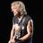 Pixelated image of a person with short light-colored hair wearing a sleeveless dark top, standing against black background.