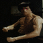 Pixelated static image of a shirtless muscular figure with red eyes, dark background, and visible pixelation artifacts.