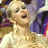 Animated sequence of a woman with blonde hair in an updo wearing a white dress, smiling broadly against a purple and brown background.