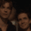 Two people in dark clothing appear in a split-screen view with a purple pixelated banner displaying partial text below.