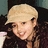 A pixelated image split into two sections: a person with light hair wearing a beige cap on the left, and blue text on a pink background on the right.