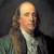 Static pixelated portrait of a person with long light brown hair, wearing a white cravat and dark coat over a green garment against a dark background.