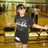 Pixelated figure in dark gray t-shirt with white graphic and shorts, standing against warm-toned background with blurred shapes.