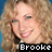 Pixelated image of a person with curly light brown hair, wearing dark clothing and holding an object near the face, with text reading 'Brooke' at bottom.