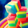A stack of colorful, striped, sugar-coated candy pieces with visible layers of red, orange, yellow, green, blue, and white arranged in a vertical cluster.
