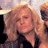 Pixelated static image of a person with long wavy blonde hair wearing dark clothing against a light background.