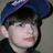 A pixelated image shows a person wearing a dark blue cap with purple trim, positioned next to a solid blue background containing partially visible text.