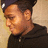 Pixelated close-up of a person wearing dark clothing and a cap, with light-colored background.