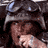 Pixelated static image of a person with dark hair wearing a helmet-like object, partially obscured by low resolution and compression artifacts.