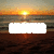 Sunset over water with a bright sun, orange and yellow sky, and dark water reflecting the sun's light.
