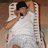 A pixelated figure in a white sleeveless shirt and dark cap holds a microphone, positioned against a light-colored structure with vertical slats.