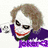 Pixelated image of a character with white face paint, red lips, and brown hair wearing a purple jacket over a green shirt.