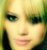 Pixelated close-up of a person's face with light skin, dark eyes, and blonde hair against green background.