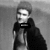 Pixelated grayscale image of a person with short hair wearing dark clothing and holding an object near the face.