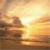 A static pixelated image depicts a sunset over water with warm orange and yellow tones, featuring a bright sun near the horizon and dark silhouettes of landmasses.