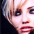 Pixelated close-up of a person's face with light-colored hair, dark eyes, and red lips against a dark background.