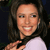 Pixelated close-up of a person with dark hair wearing a white top, smiling with visible teeth against a dark background.