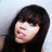 Pixelated static image of a person with long dark hair, closed eyes, and a slightly open mouth against a light gray background.