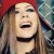 Pixelated static image of a person with long hair and red headwear, mouth open in laughter or shouting, against a multicolored background.