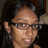 Pixelated close-up of a person with dark hair, glasses, and light skin tone against a dark background.