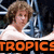 Pixelated image of a person with light brown curly hair wearing a white shirt, positioned next to a blue and silver object with orange text reading 'TROPICS' at the bottom.