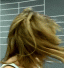 A woman with light brown hair in motion, wearing a white tank top and black necklace, against a gray background