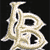 A pixelated, stylized letter B in beige and white tones on a black background, with a decorative, ornate design featuring curved lines and negative space.