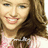 A pixelated close-up of a smiling person with long brown hair wearing a light pink top, cropped to show only the upper body.