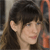 A pixelated close-up of a person with dark hair and bangs, showing the ear and part of the face against a blurred background.
