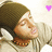 A person wearing a brown knit beanie and light gray hoodie with white earphones, eyes closed in relaxed expression.