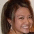 A person with shoulder-length brown hair and light skin smiles broadly, showing teeth in three