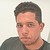 Static pixelated image of a person with short dark hair, light skin, and a dark shirt against a light background.