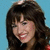 A woman with brown hair and bangs smiles against a blue background, wearing red clothing.
