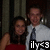 Two people pose together in a dimly lit indoor setting; one wears a red sleeveless top, the other a light shirt and dark tie, with text overlay reading 'ily<3' at the bottom center.