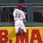 A pixelated image of a baseball player in white uniform jumping over a yellow wall with red letters, next to blue text on red background.