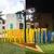 Pixelated static image showing a yellow structure with vertical elements, green ground, and light sky background.