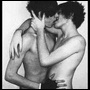 Black-and-white static image of two shirtless individuals embracing in a close, intimate pose with one person's hand near the other's face.