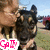 A person holds a dog in an outdoor setting with a grassy field and vehicles in the background, while text overlays change across frames.