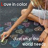 A person in light shorts draws colorful heart shapes on a dark surface with chalk, text reads "Love in color" and "Just what the world needs".