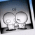 Two stylized cartoon heads with large circular eyes and simple facial features, one holding a small object near its mouth against a gradient background.