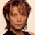 Pixelated portrait of a person with light brown hair styled in a side-swept manner, wearing a dark top against a light background.